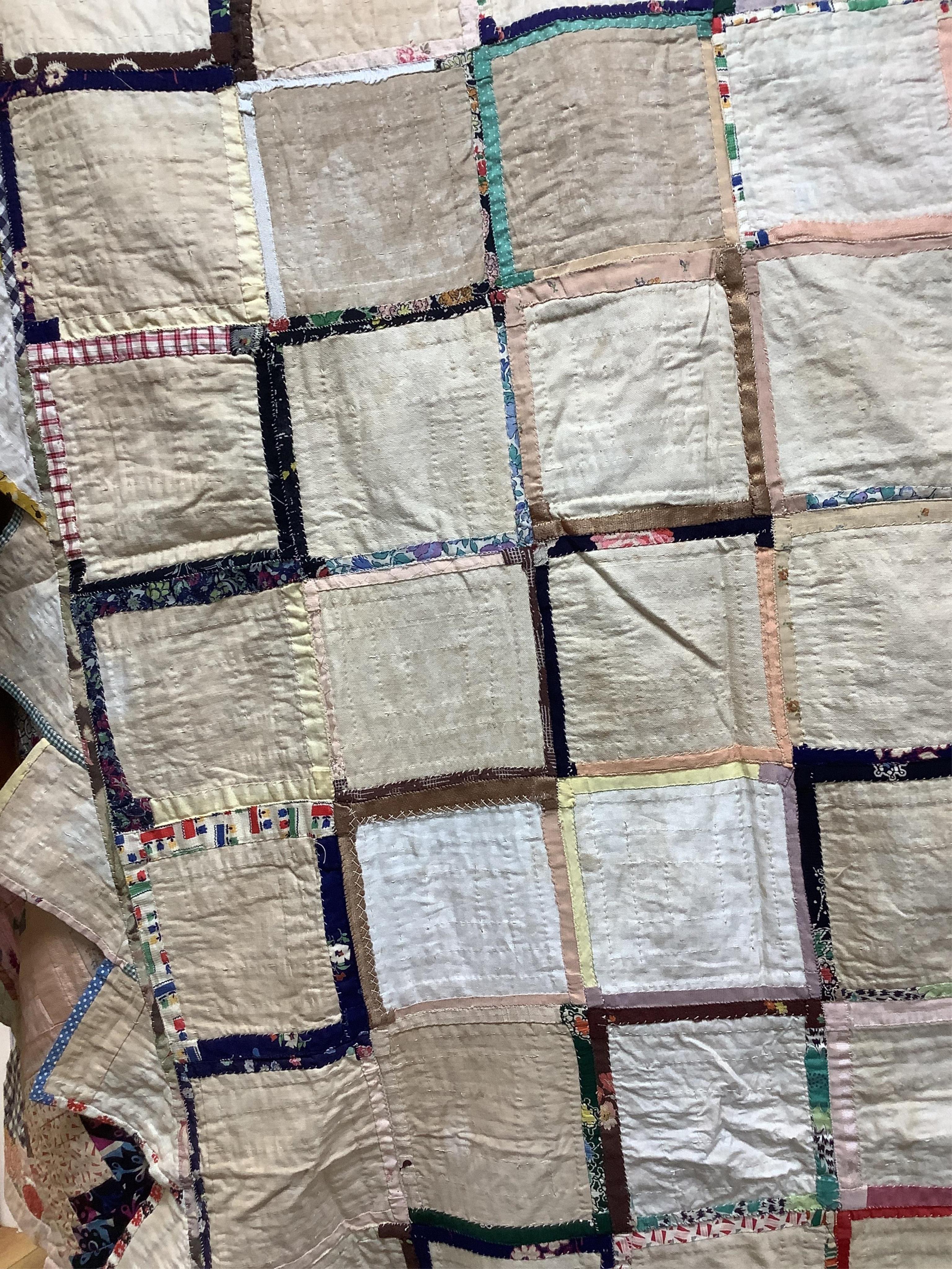 An early 20th century Log Cabin patchwork bedcover, worked in plain and printed silk, rayons and cottons from 1900 to 1940’s. Edged with a triangular patchwork border on three sides. Cover unlined. 158cm wide x 192cm lon